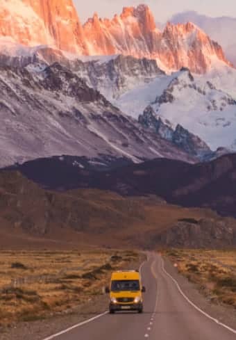 Patagonya'da karlı Fitz Roy masifinin altındaki açık bir yolda sarı kampçı minibüsü